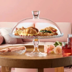 Patera na nóżce z kloszem Patisserie Pasabahce 32 cm postawiona na stole, wewnątrz drożdżówki.