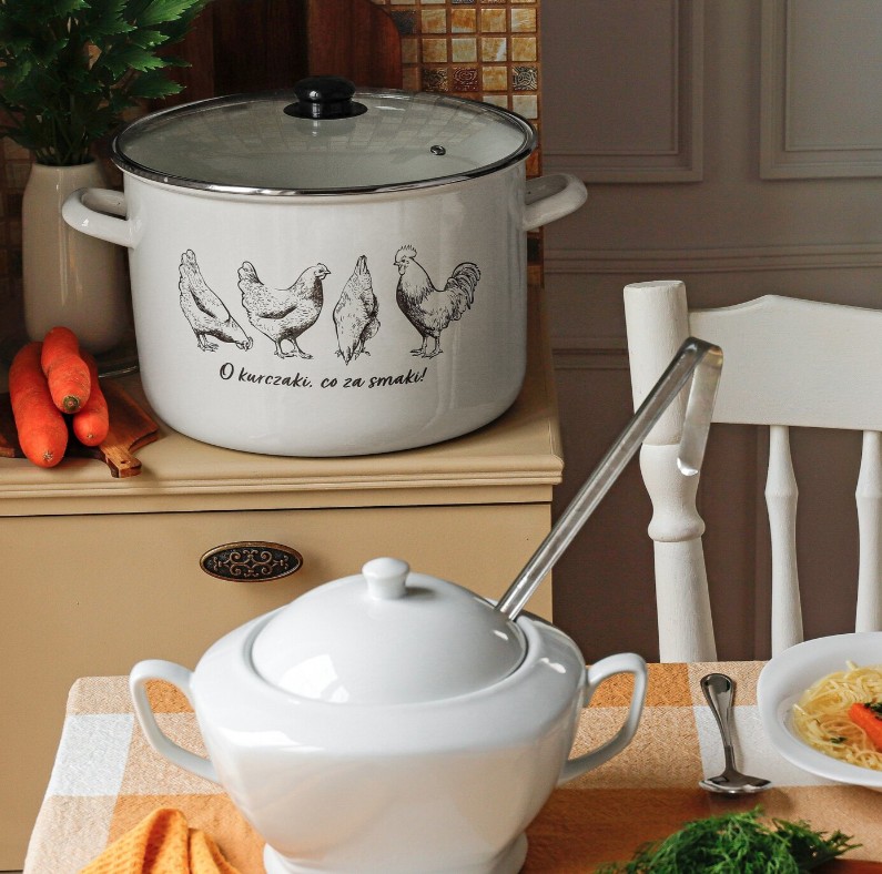 Emaliowany garnek z pokrywką i motywem kurczaków oraz biała ceramiczna waza na stole w przytulnej, rustykalnej kuchni. Obok talerz z rosołem. Klasyczne naczynia kuchenne w stylu retro, idealne do gotowania i serwowania potraw.